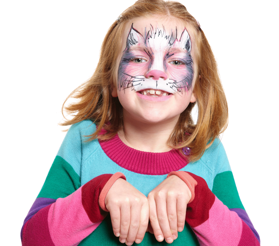 A photo of a young person with cat face painting. They have shoulder-length, light brown hair, are pale skinned and are smiling at the camera.