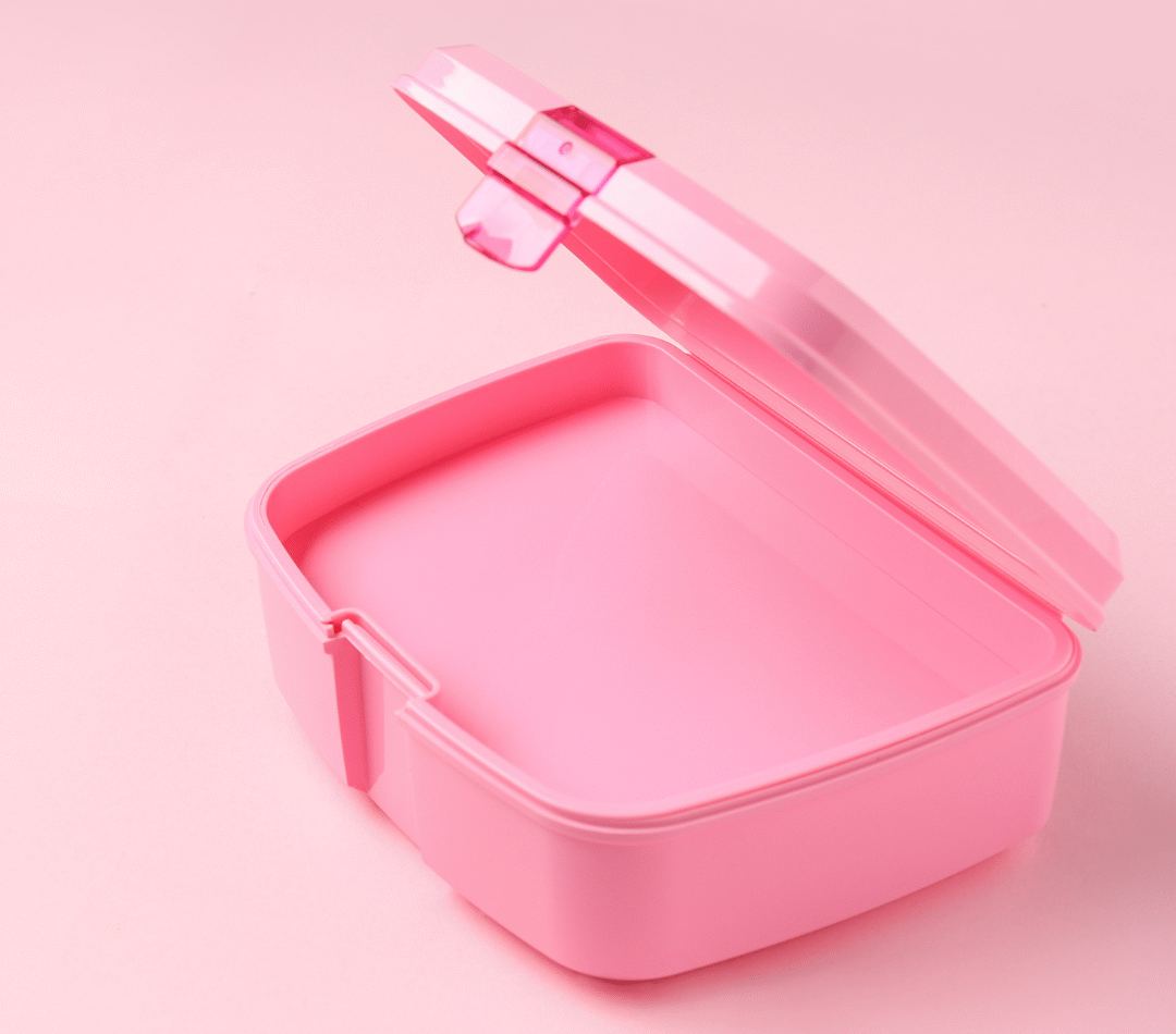 An empty, pink lunch box in front of a pink background