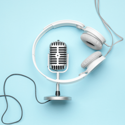 A podcasting, silver microphone with a set of white headphones are against a light blue backdrop