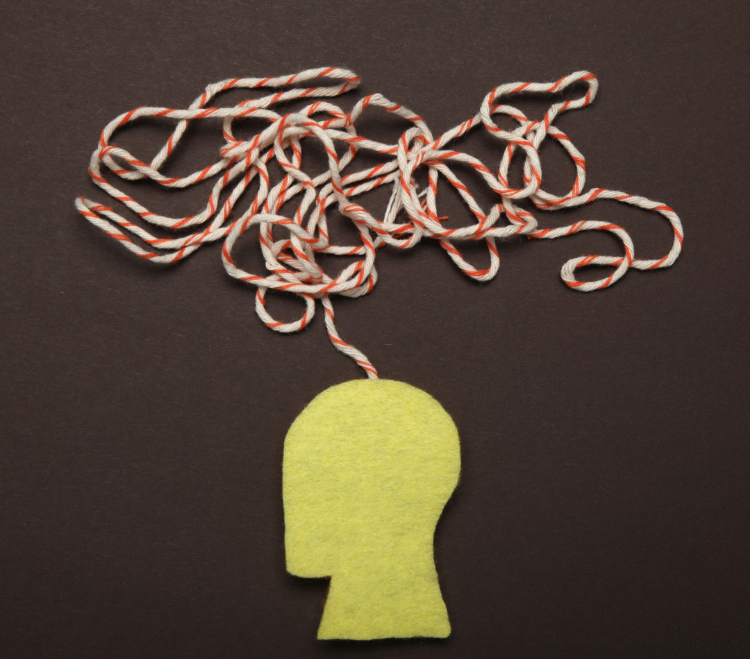 An image depicting a silhouette of a person's head with yellow felt and then red and white yarn coming out as tangled thoughts from their head.