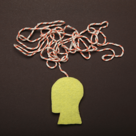 An image depicting a silhouette of a person's head with yellow felt and then red and white yarn coming out as tangled thoughts from their head.