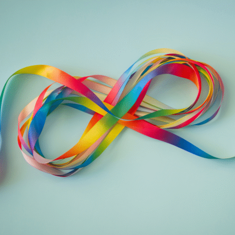 A photo of a rainbow coloured ribbon in the shape of the infinity symbol.