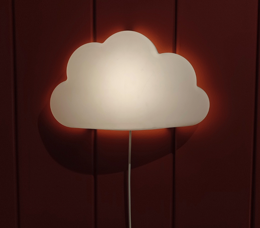 A cloud shaped night light hanging on a red wall.